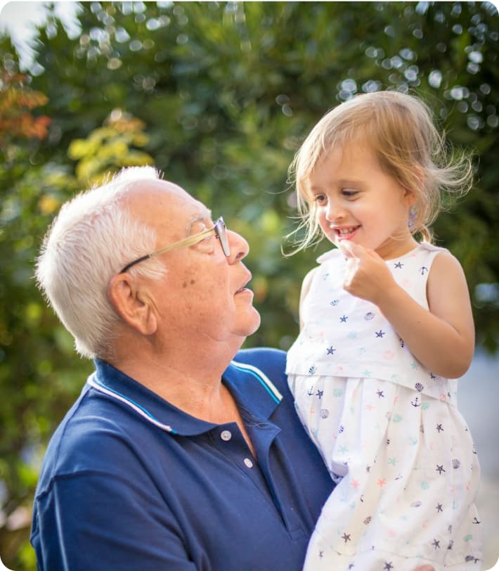 A grandfather holding his smiling granddaughter outdoors